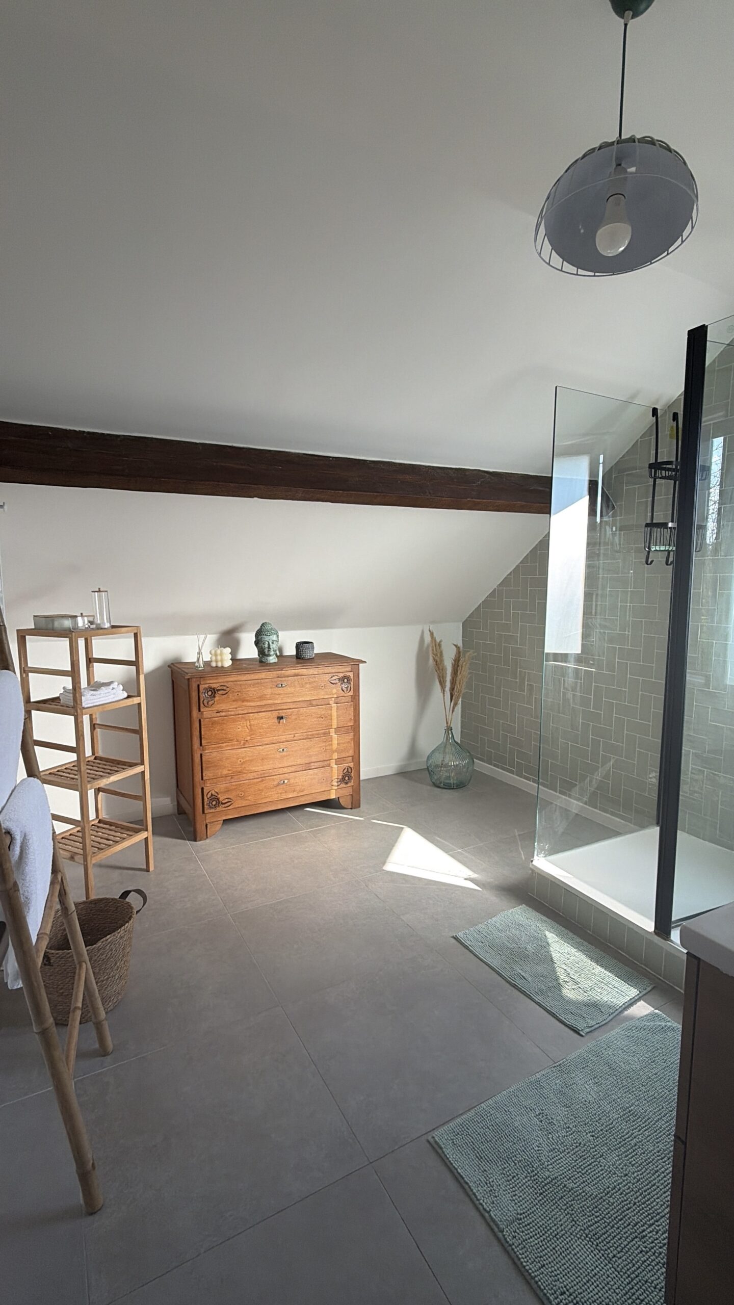 Salle de bain sous combles mêlant commode ancienne en bois, douche verrière moderne noire et carrelage vert sauge artisanal