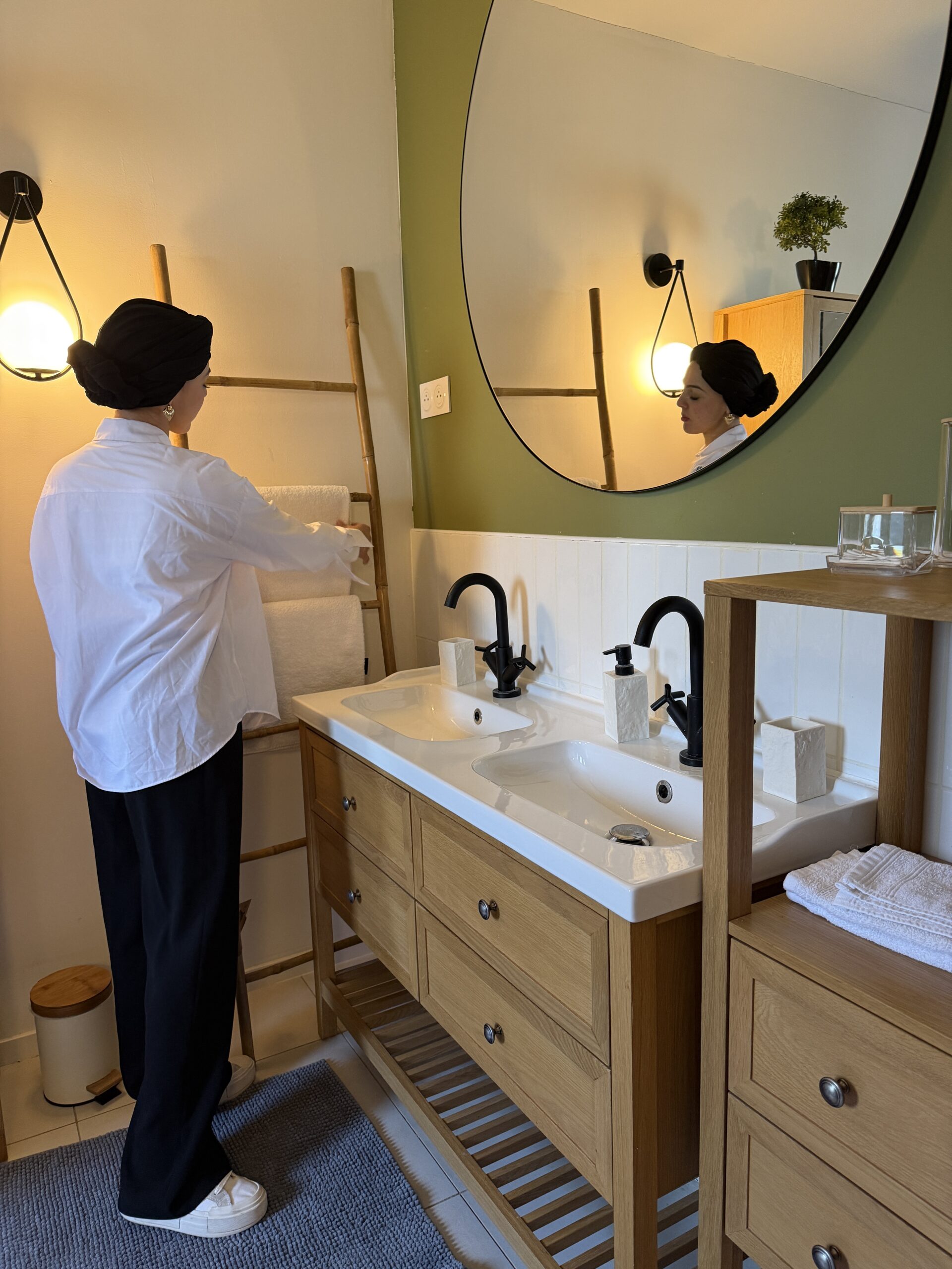 Salle de bain California Farmhouse — murs vert sauge, meuble vasque en chêne, robinetterie noire mate et échelle en bambou